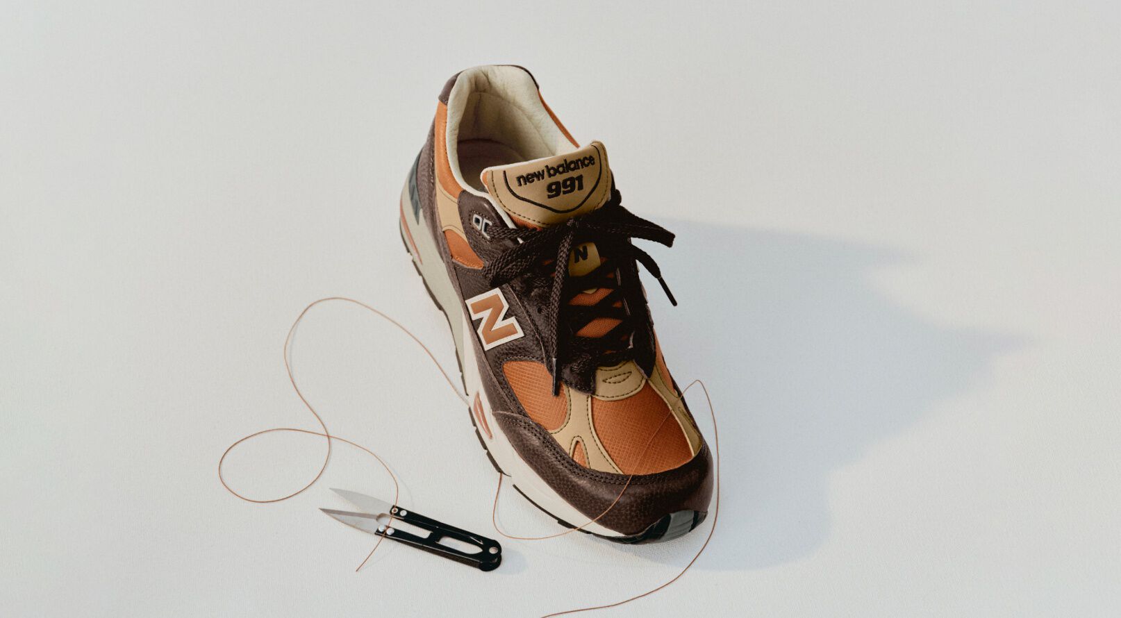A New Balance Made in UK sneaker in a white studio environment next to sewing thread and fabric shears. 