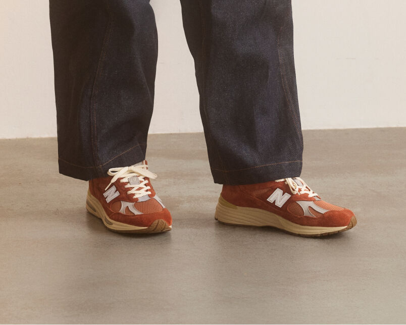 A pair of New Balance Made in UK sneakers in front of a rabbit in a brown textured studio environment. 