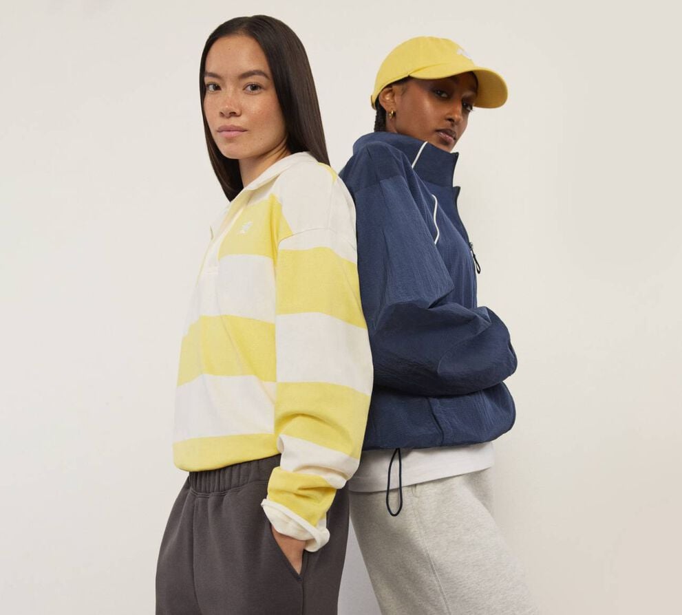 Two woman wearing New Balance standing back to back and looking at the viewer.