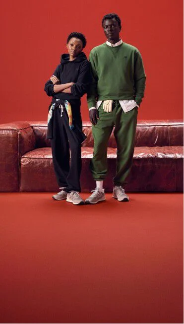 Couple wearing same color outfits standing on a red background in front of a red couch.