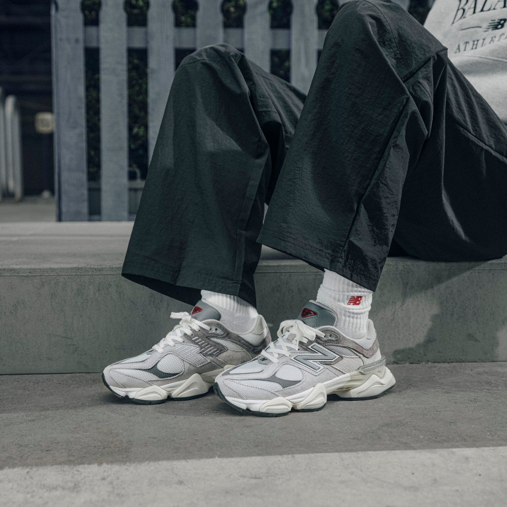 A person sitting wearing grey New Balance 9060's