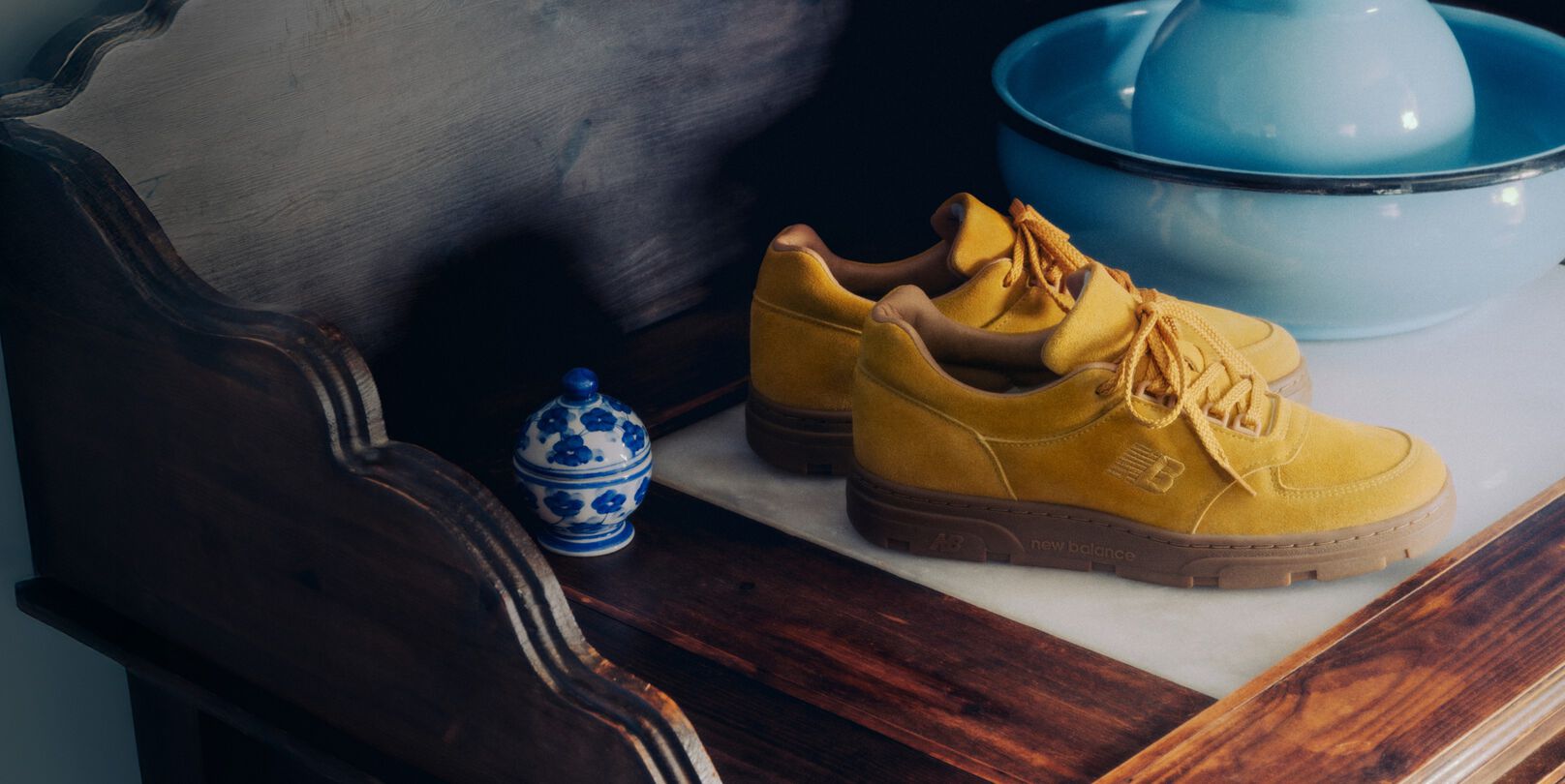 A pair of New Balance Made in UK sneakers on an antique wooden dresser next to a selection of vases. 