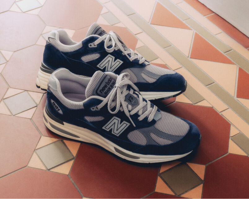 A pair of New Balance Made in UK sneakers on a white workbench surrounded by shoemaking tools and other textile equipment. 
