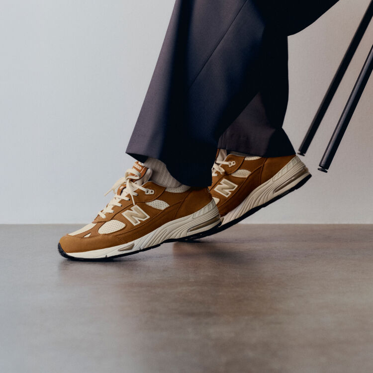 Knee down view of a man wearing a pair of New Balance Made in UK sneakers in with room with a concrete floor and white walls. 