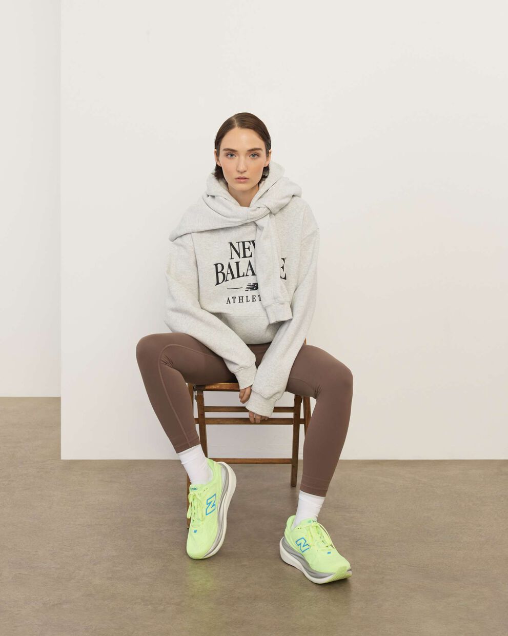 A woman wearing New Balance sitting in a chair in front a white wall.